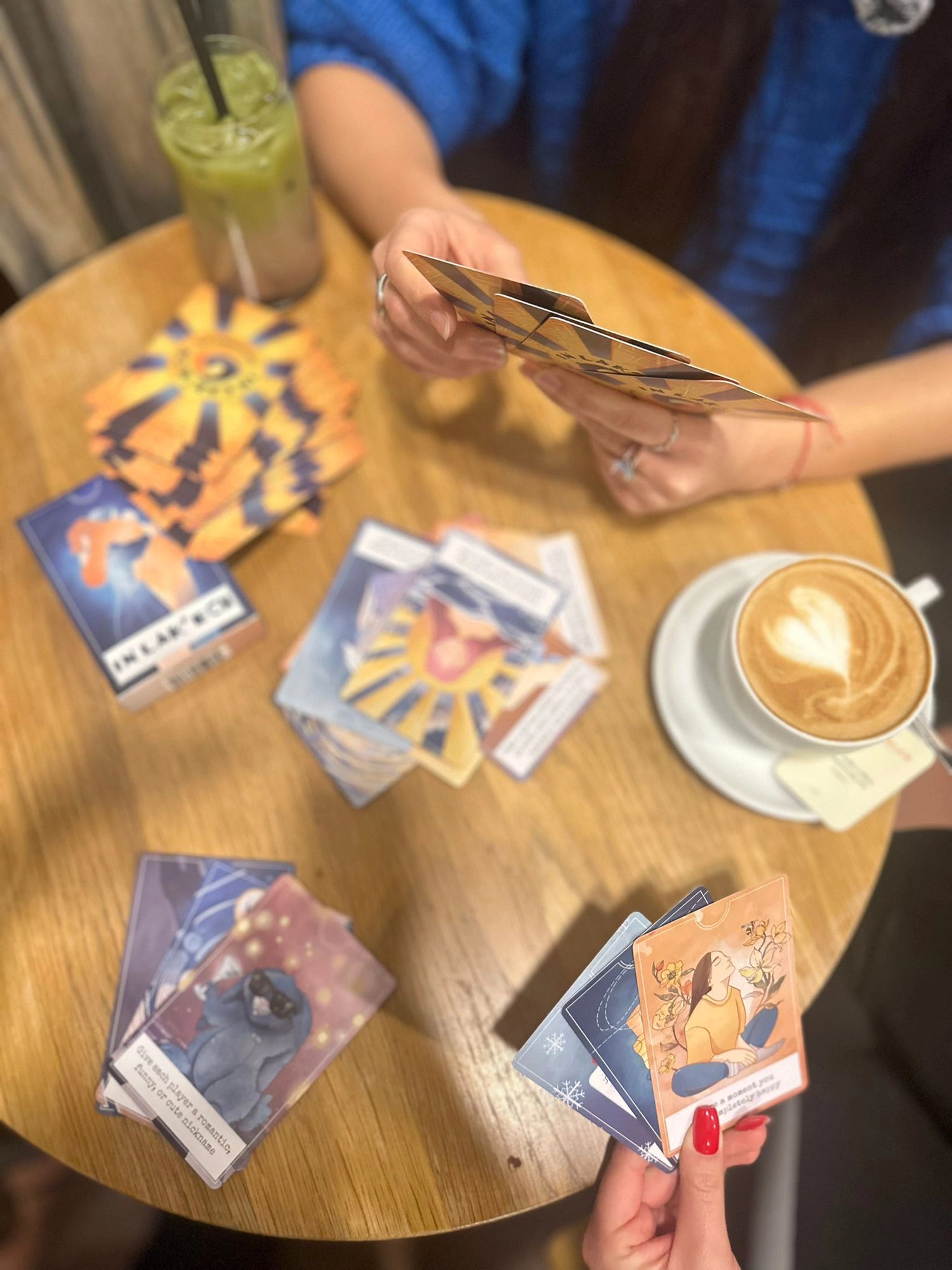 Two people playing In Lak'ech at a table with cards and drinks.
