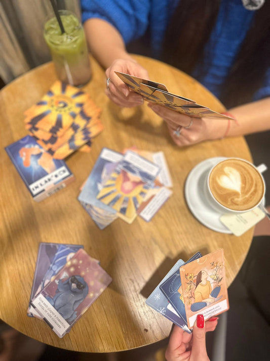 Two people playing In Lak'ech at a table with cards and drinks.